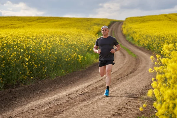 Biegacz Średnim Wieku Biegający Polnej Drodze Kwitnącym Polu Rzepakowym — Zdjęcie stockowe