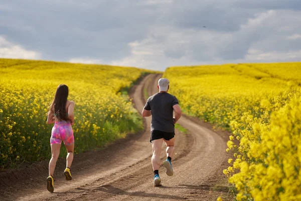 Bir Çift Koşucu Bir Kanola Tarlasında Toprak Bir Pistte Tepe — Stok fotoğraf