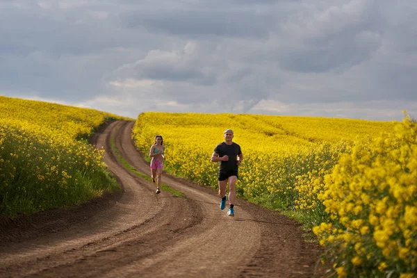 Bir Çift Koşucu Bir Kanola Tarlasında Toprak Bir Pistte Tepe — Stok fotoğraf