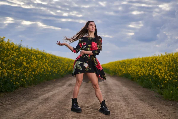 春の終わりに菜の花畑で花のドレスを着た美しいヒスパニック系の若い女性の肖像画 — ストック写真