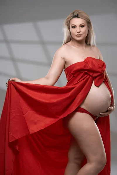 美しいです妊娠若いですブロンド女性で赤波シート上の灰色の背景 — ストック写真