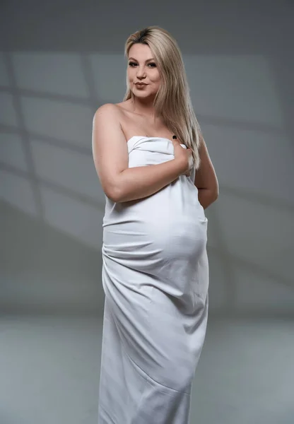 美しいです妊娠若いですブロンド女性でホワイトシート上のグレーの背景 — ストック写真