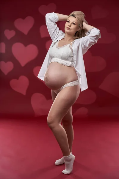 美しいです妊娠若いですブロンド女性でホワイトランジェリー上の赤背景 — ストック写真