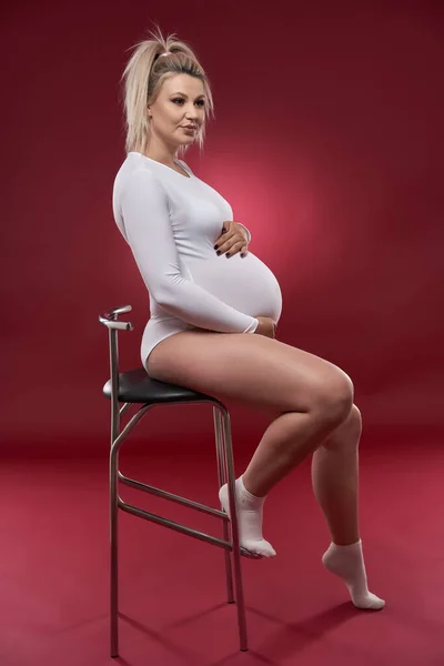 Krásná Těhotná Mladá Blondýna Žena Bílém Prádle Pózovat Červeném Pozadí — Stock fotografie