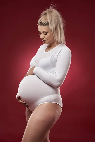美しいです妊娠中の若いですブロンド女性でホワイトランジェリーポーズオン赤背景 — ストック写真