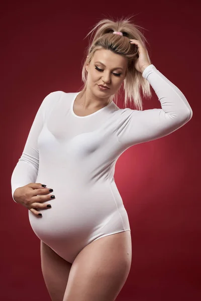 美しいです妊娠中の若いですブロンド女性でホワイトランジェリーポーズオン赤背景 — ストック写真