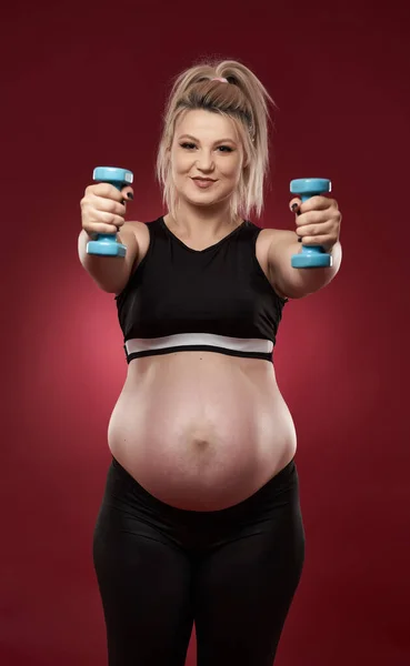 若いです妊娠中の女性は 赤の背景にフィットネス演習を行います スタジオショット — ストック写真