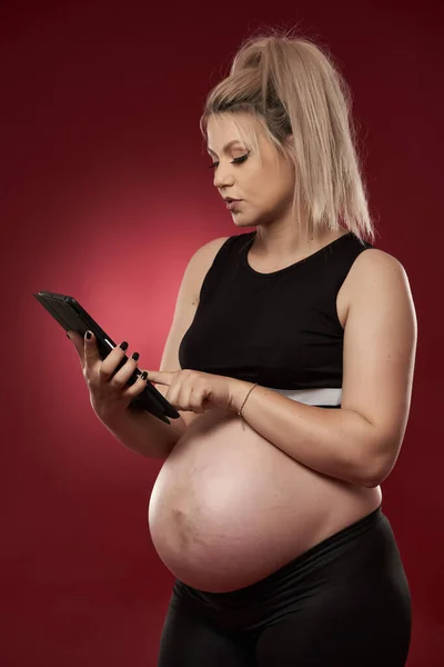 Hamile Kadın Tablet Kullanıyor Stüdyo Fotoğrafı Kırmızı Arka Planda — Stok fotoğraf