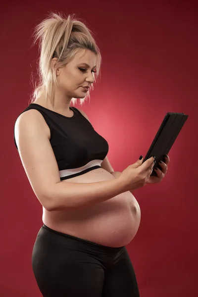 Kobieta Ciąży Pomocą Tabletu Studio Strzał Czerwonym Tle — Zdjęcie stockowe