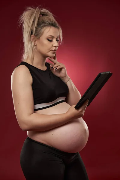 Mulher Grávida Usando Tablet Estúdio Filmado Fundo Vermelho — Fotografia de Stock