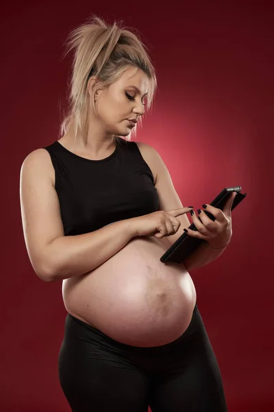 Kobieta Ciąży Pomocą Tabletu Studio Strzał Czerwonym Tle — Zdjęcie stockowe