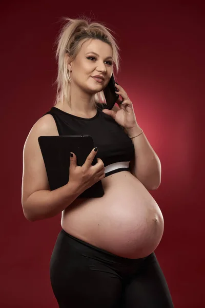 Беременная Женщина Говорит Мобильному Телефону Студия Снимается Красном Фоне — стоковое фото
