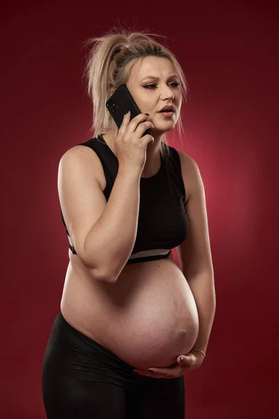 Zwangere Vrouw Spreken Mobiele Telefoon Studio Schot Rode Achtergrond — Stockfoto