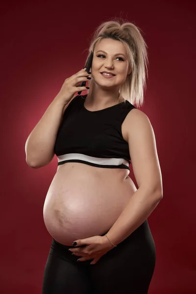 Těhotná Žena Mluví Mobilním Telefonu Studio Shot Červeném Pozadí — Stock fotografie