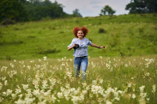 Woman nature photographer happy and cheerful, running with camera on a meadow