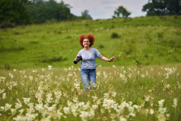 女性の自然写真家は幸せと陽気で 牧草地でカメラを持って走っている — ストック写真