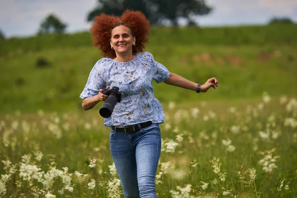 女性の自然写真家は幸せと陽気で 牧草地でカメラを持って走っている — ストック写真