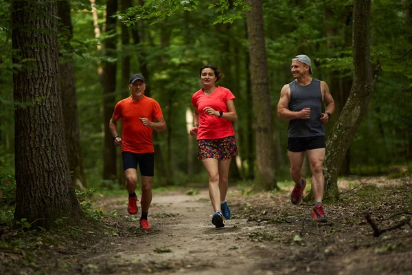 三人一组 跑步穿过森林 沿着小径跑 — 图库照片