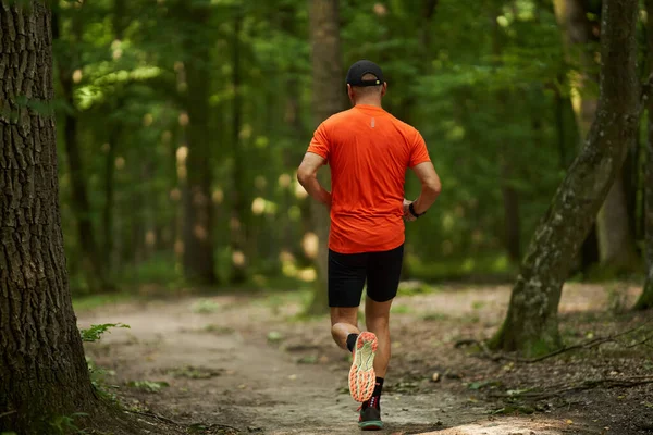A caucasian man jogging on a running trail through the forest
