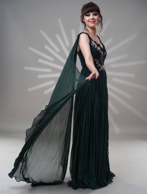 Koyu yeşil elbiseli, gri arka planda çok güzel bir kadın.