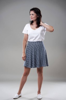 Gri arka planda günlük kıyafet giymiş esmer bir kadını cezbediyor.