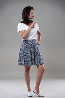 Gri arka planda günlük kıyafet giymiş esmer bir kadını cezbediyor.