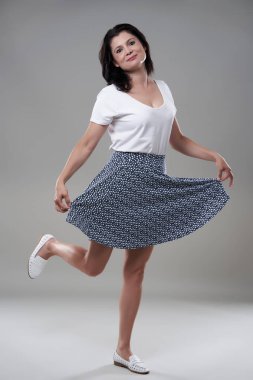 Gri arka planda günlük kıyafet giymiş esmer bir kadını cezbediyor.