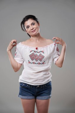 Kısa kotlu ve gri arka planda çiçekli bluzlu mutlu esmer kadın.