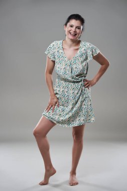 Gri arka planda günlük kıyafet giymiş esmer bir kadını cezbediyor.