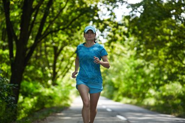 Ormanda asfalt yolda koşan kadın koşucu