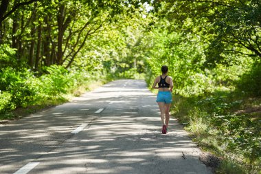 Ormanda asfalt yolda koşan kadın koşucu
