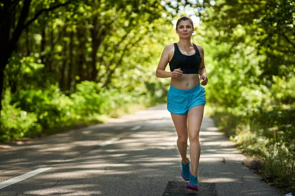 女性ランナー 森のアスファルト道路でジョギング ロイヤリティフリーのストック写真