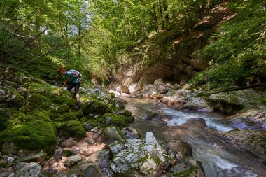 Sırt çantalı bir kadın yürüyüşçü nehir kenarındaki vahşi geçitleri keşfediyor. Kocaman yosun kaplı kayalar.