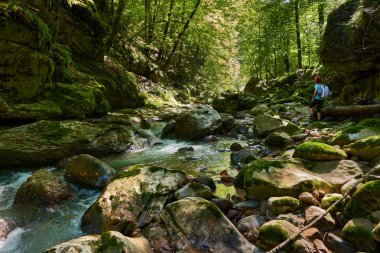 Sırt çantalı bir kadın yürüyüşçü nehir kenarındaki vahşi geçitleri keşfediyor. Kocaman yosun kaplı kayalar.