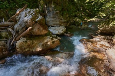 Sırt çantalı bir kadın yürüyüşçü nehir kenarındaki vahşi geçitleri keşfediyor. Kocaman yosun kaplı kayalar.