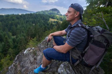 Yürüyüşçü dağın tepesinde güzel bir manzarayla dinleniyor.