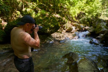 Gömleksiz sporcu doğa fotoğrafçısı bir kanyonda nehir ve akıntıyla fotoğraf çekiyor.