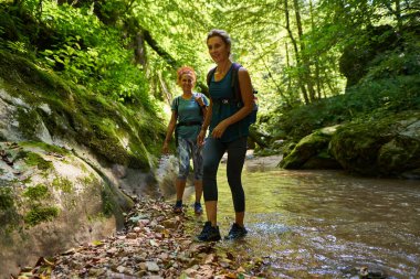 Sırt çantalı kadın yürüyüşçüler yemyeşil bir kanyonu ve nehri keşfediyorlar.