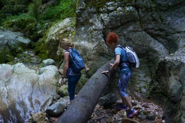 Sırt çantalı kadın yürüyüşçüler yemyeşil bir kanyonu ve nehri keşfediyorlar.