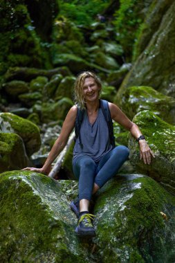 Sırt çantalı bir kadın gezgin, içinde nehir olan yemyeşil bir kanyonu keşfediyor.