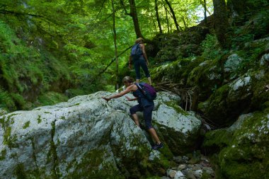 Sırt çantalı kadın yürüyüşçüler yemyeşil bir kanyonu ve nehri keşfediyorlar.