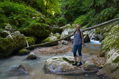 Sırt çantalı bir kadın gezgin, içinde nehir olan yemyeşil bir kanyonu keşfediyor.