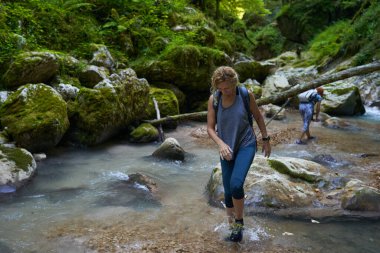 Sırt çantalı kadın yürüyüşçüler yemyeşil bir kanyonu ve nehri keşfediyorlar.