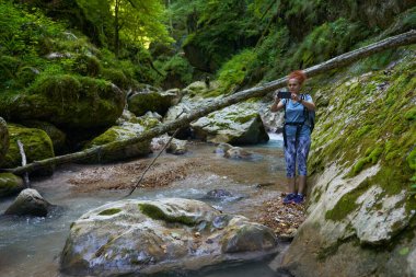 Sırt çantalı bir kadın gezgin, içinde nehir olan yemyeşil bir kanyonu keşfediyor.