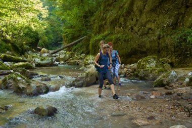Sırt çantalı kadın yürüyüşçüler yemyeşil bir kanyonu ve nehri keşfediyorlar.