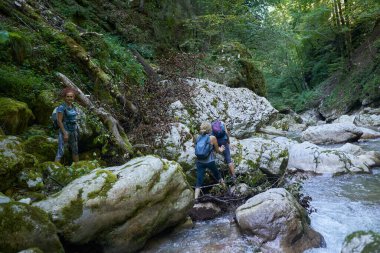 Sırt çantalı kadın yürüyüşçüler yemyeşil bir kanyonu ve nehri keşfediyorlar.