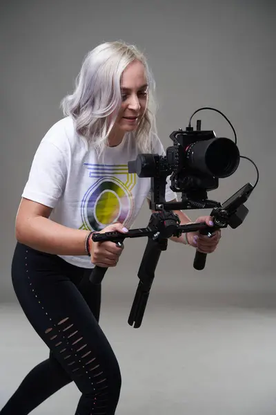 Woman videographer with cinema camera on gimbal on gray background