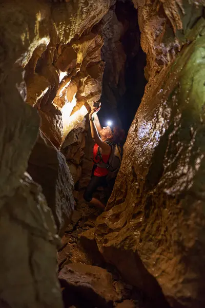 Woman with backpack and head torch exploring a cave and taking pictures