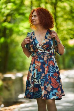 Parktaki çiçekli elbiseli güzel, kıvırcık saçlı bir kadının portresi.