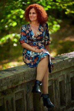 Parktaki çiçekli elbiseli güzel, kıvırcık saçlı bir kadının portresi.